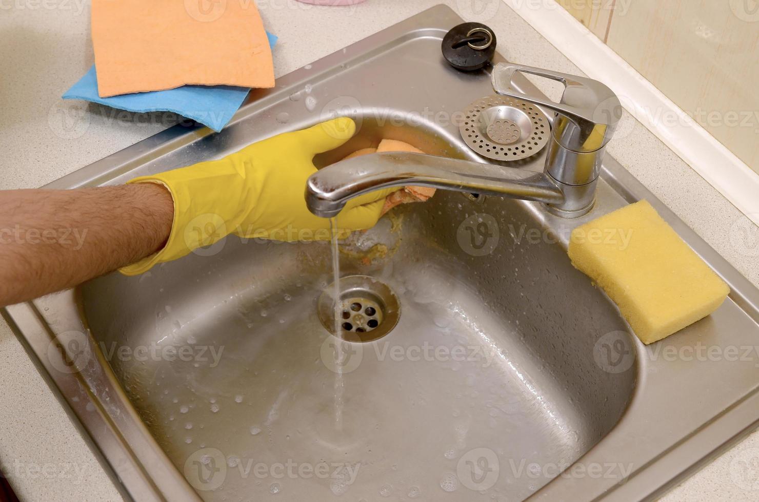 Person or householder cleaning the kitchen sink with sponge in close up view photo