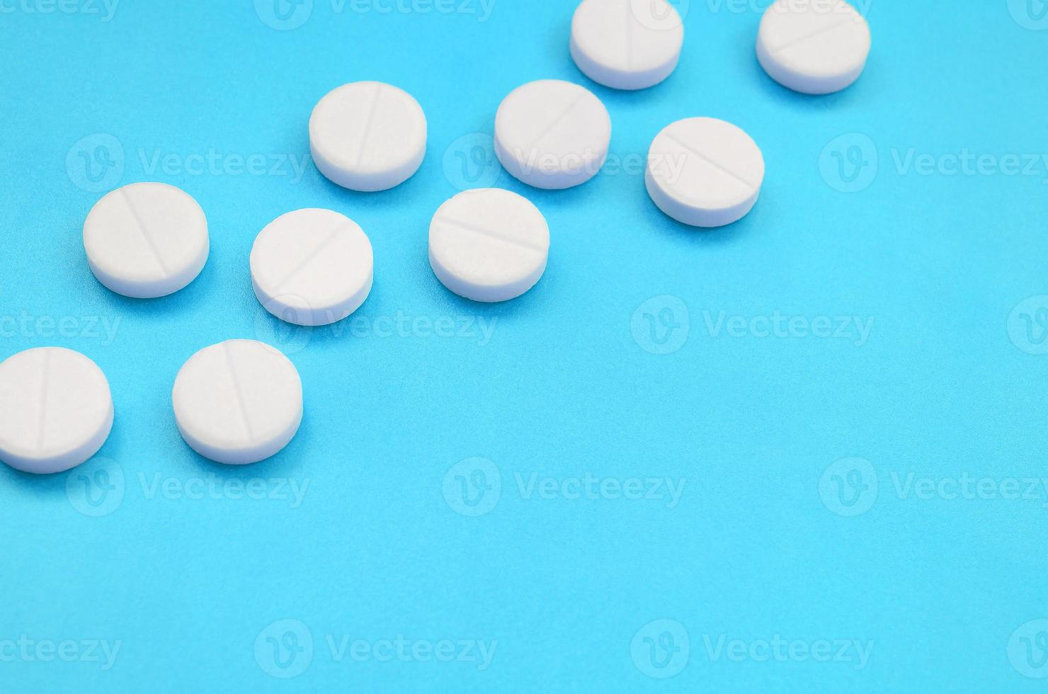 A few white tablets lie on a bright blue background surface. Background image on medical and pharmaceutical topics photo