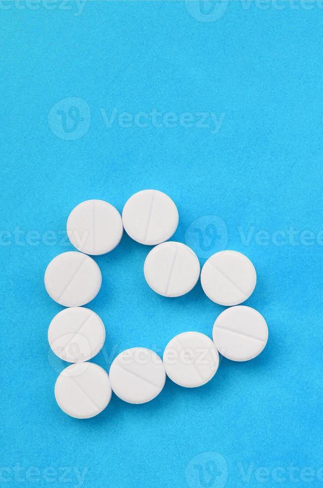 Several white tablets lie on a bright blue background in the shape of a heart. Background image on medicine and pharmaceutical topics photo