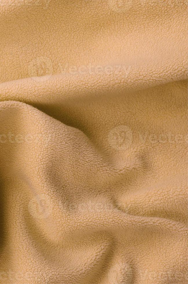The blanket of furry orange fleece fabric. A background of light orange soft plush fleece material with a lot of relief folds photo