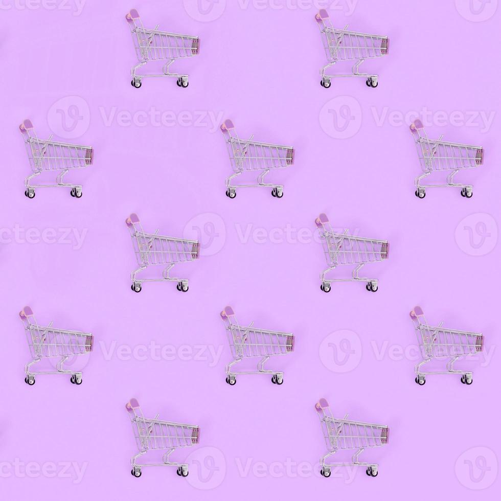 Shopping addiction, shopping lover or shopaholic concept. Many small empty shopping carts perform a pattern on a pastel colored paper background. Flat lay composition, top view photo