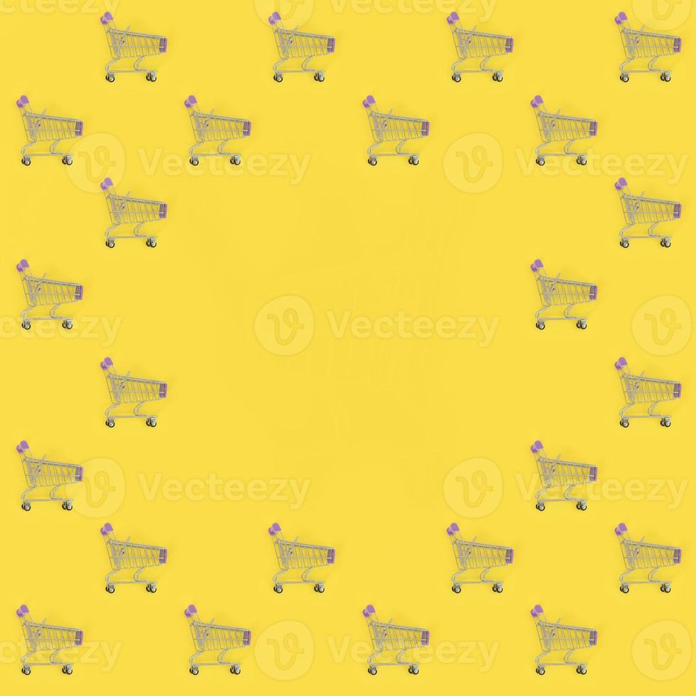 Shopping addiction, shopping lover or shopaholic concept. Many small empty shopping carts perform a pattern on a pastel colored paper background. Flat lay composition, top view photo