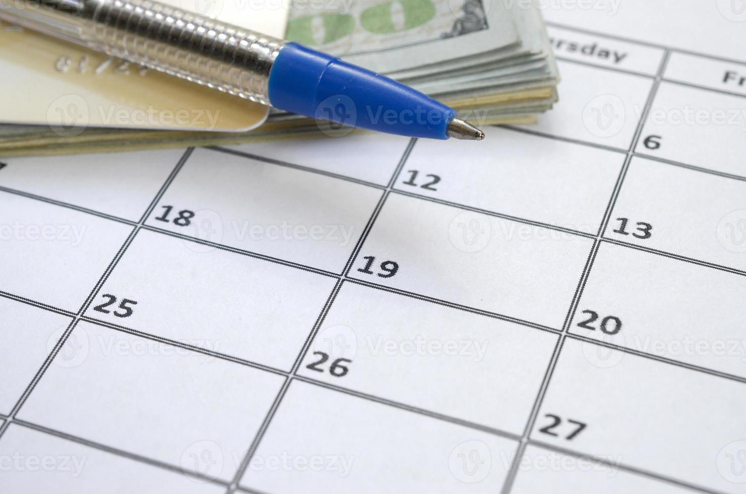 Pen and credit card on many hundred US dollar bills on calendar page close up photo