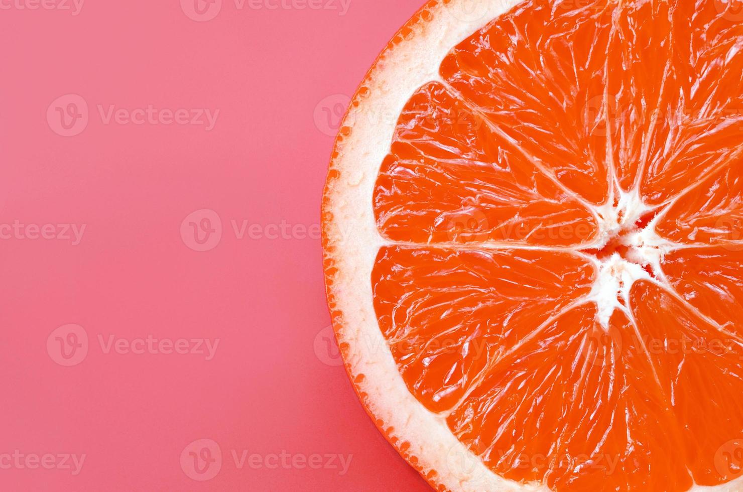 Top view of a one grapefruit slice on bright background in light pink color. A saturated citrus texture image photo