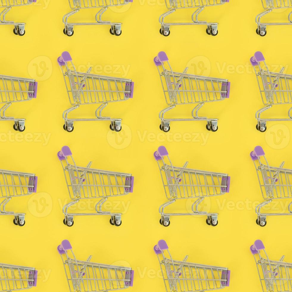 adicción a las compras, amante de las compras o concepto de adicto a las compras. muchos pequeños carros de compras vacíos realizan un patrón sobre un fondo de papel de color pastel. composición plana, vista superior foto