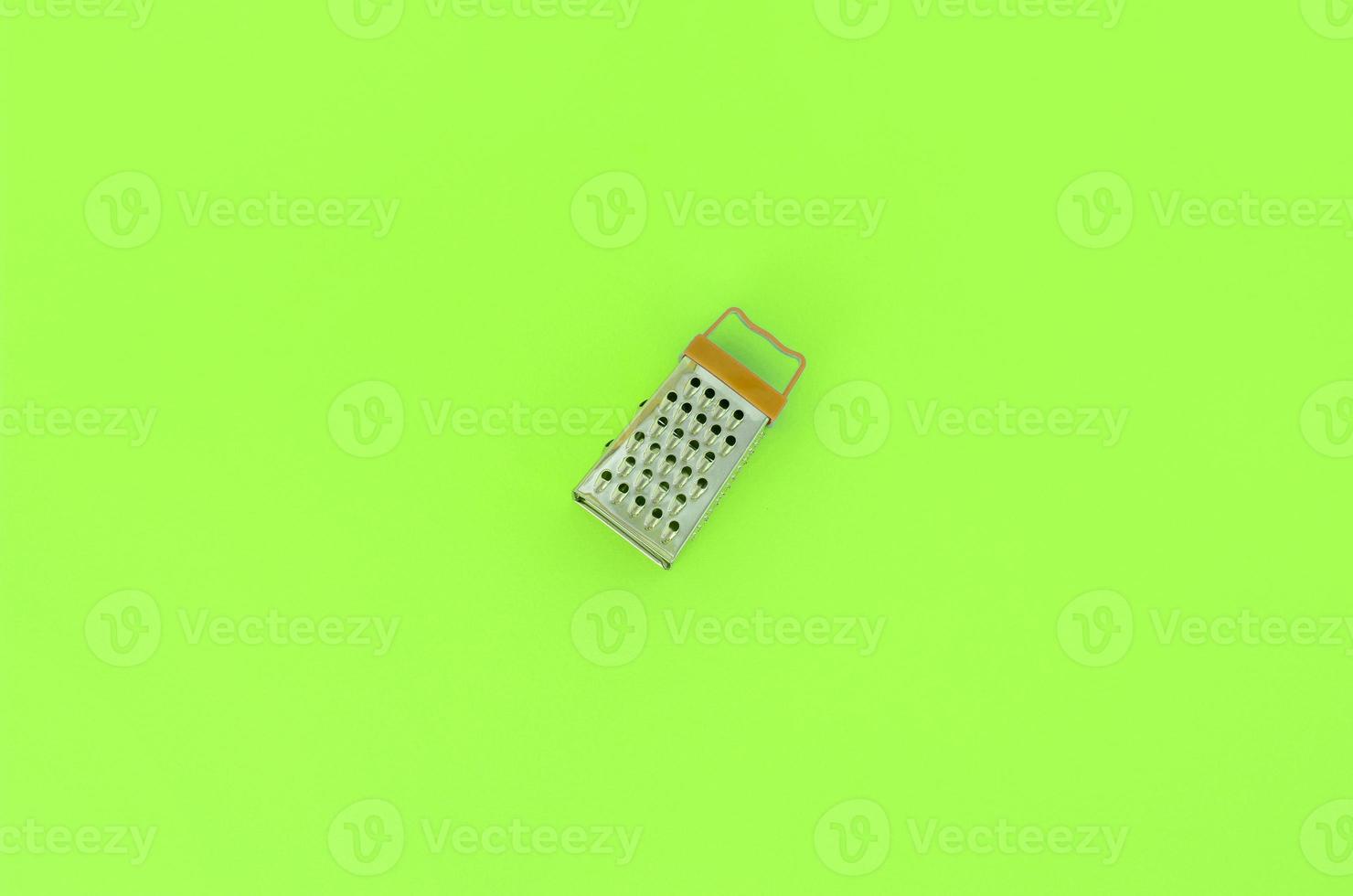 Stainless steel grater lies on a pastel colored paper. Kitchen accessories. Tools for cooking. Flat lay top view photo