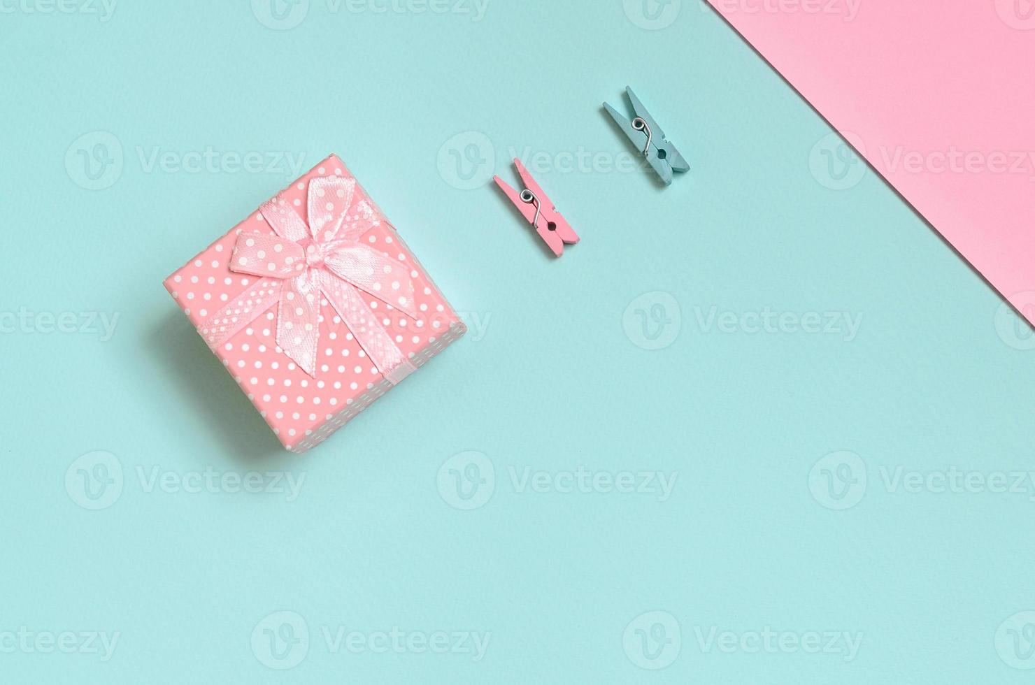 Small pink gift box and two pegs lie on texture background of fashion pastel blue and pink colors paper in minimal concept photo