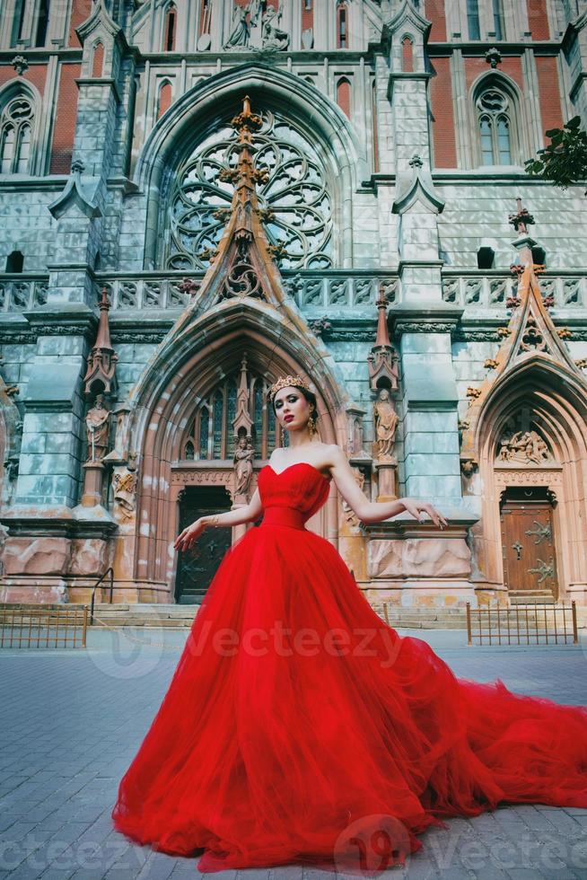 bella mujer con vestido rojo largo y corona real casi catedral católica foto