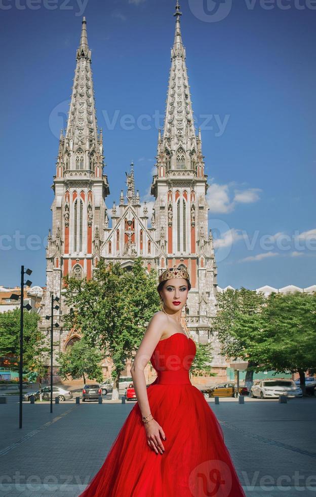 bella mujer con vestido rojo largo y corona real casi catedral católica foto