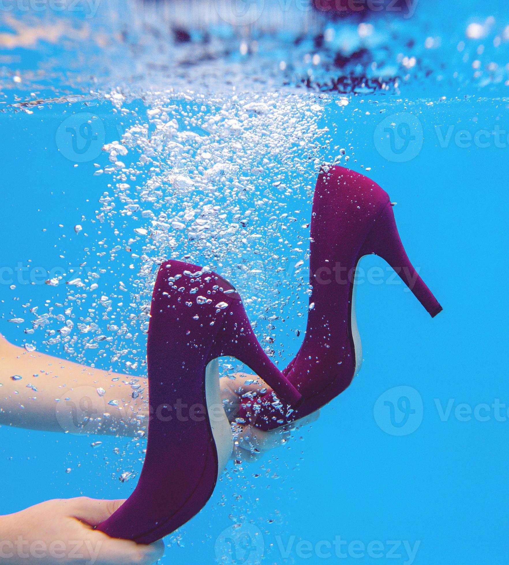 Young slim woman in gray dress holding Violet velvet shoes underwater