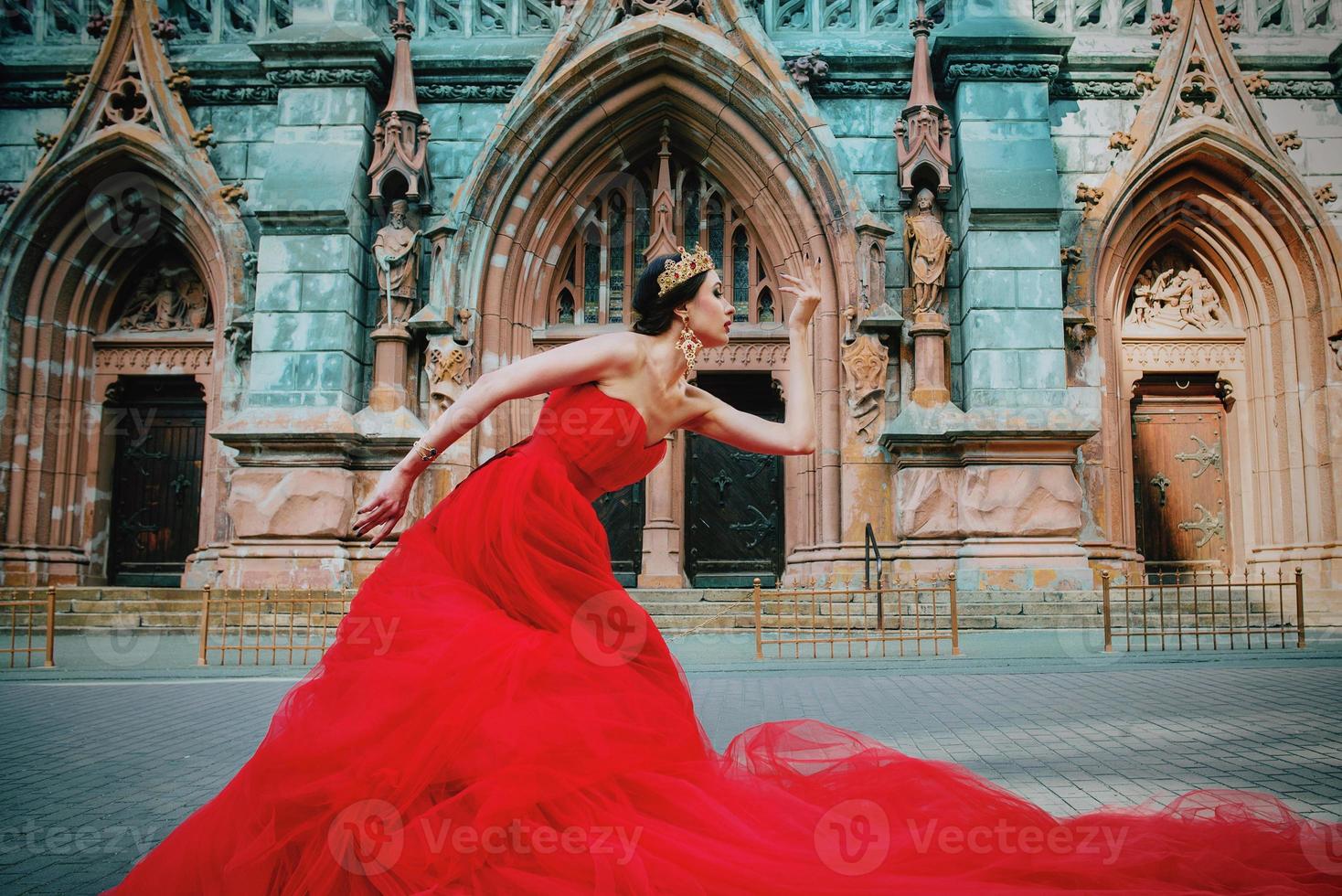 bella mujer con vestido rojo largo y corona real casi catedral católica foto