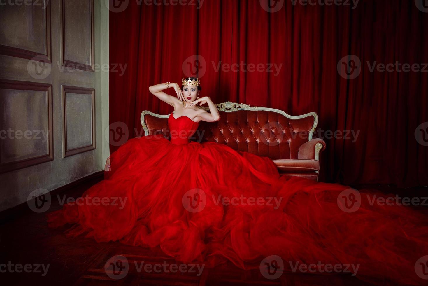 Beautiful woman in long red dress and in royal crown indoor photo