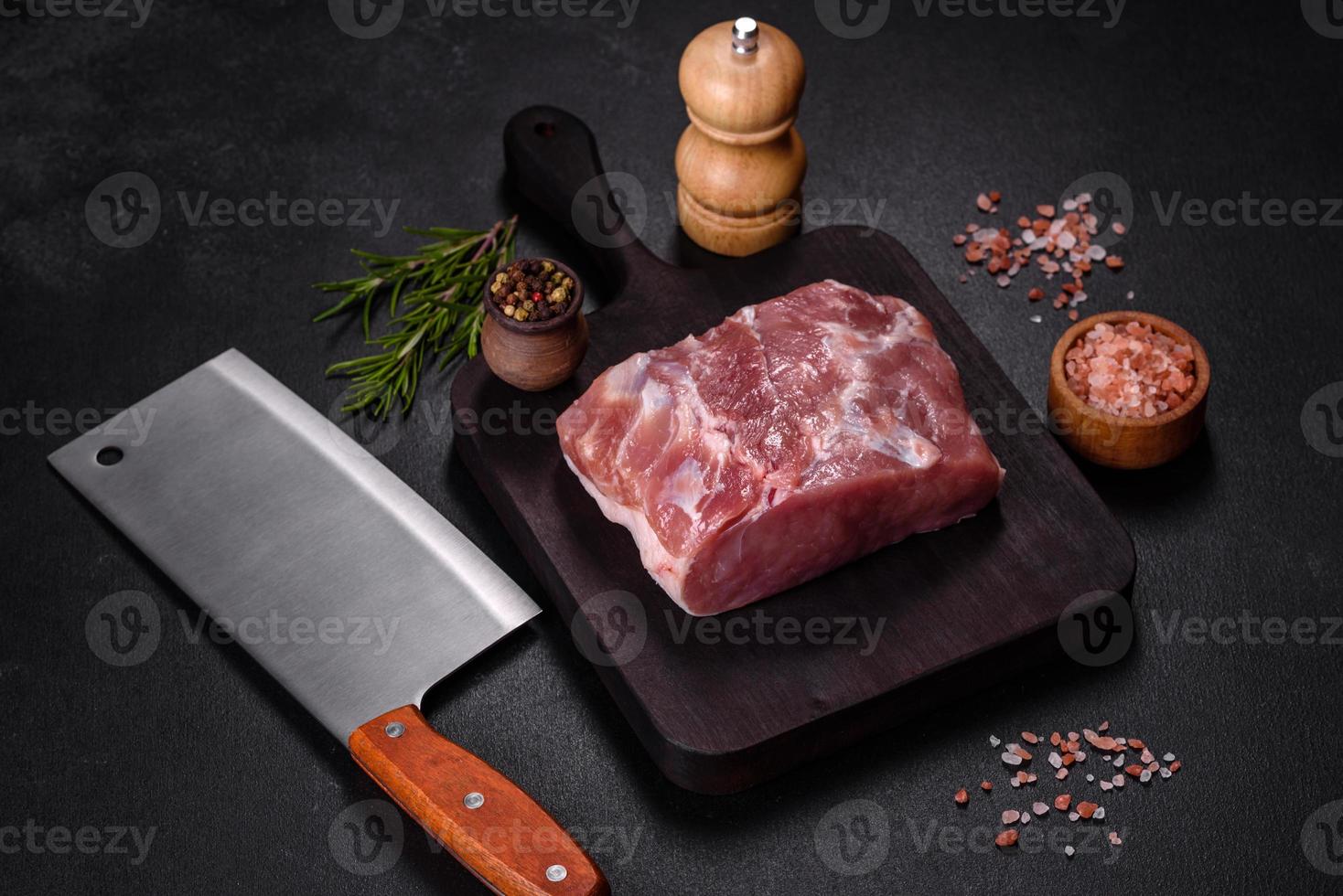 pieza fresca de cerdo crudo con especias, sal y hierbas en una tabla de cortar de madera foto