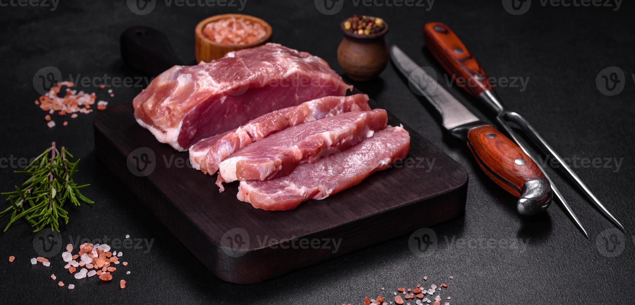 Fresh piece of raw pork with spices, salt and herbs on a wooden cutting board photo