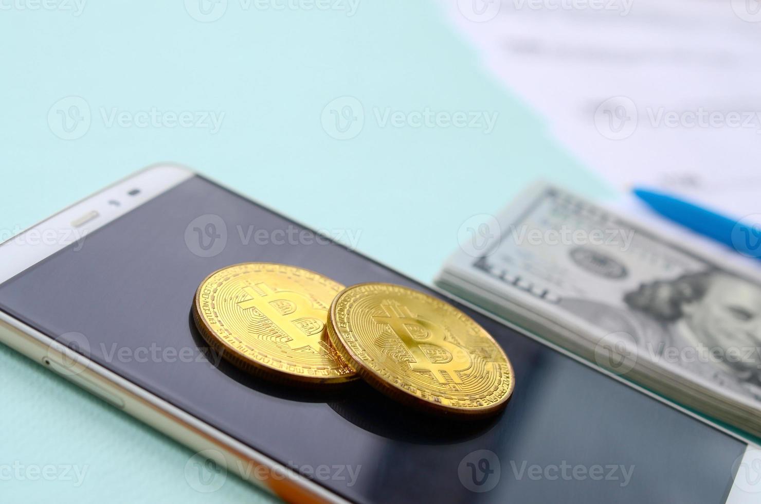 bitcoins se encuentra con los formularios de impuestos, los billetes de cien dólares y el teléfono inteligente en un fondo azul claro. declaración de la renta foto