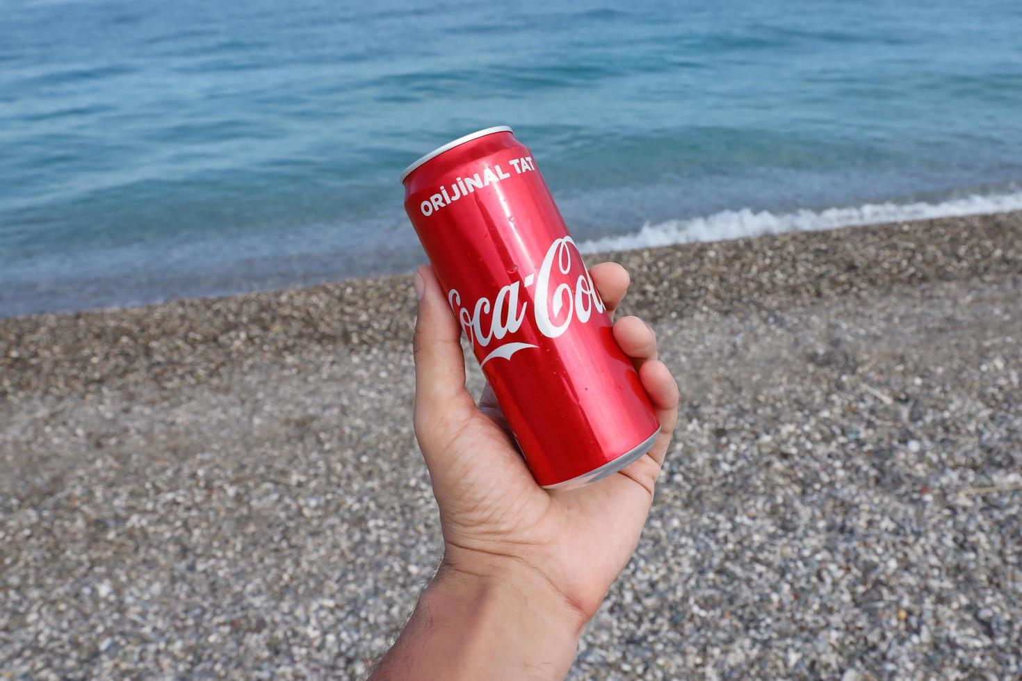 ANTALYA, TURKEY - MAY 18, 2022 Original Coca Cola red tin can lies on small round pebble stones close to sea shore. Coca-cola can in male hand on beach photo