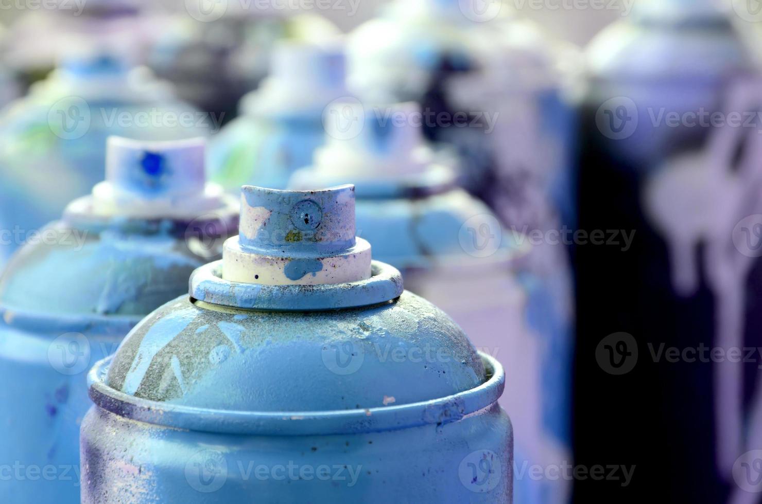 A lot of dirty and used aerosol cans of bright blue paint. Macro photograph with shallow depth of field. Selective focus on the spray nozzle photo