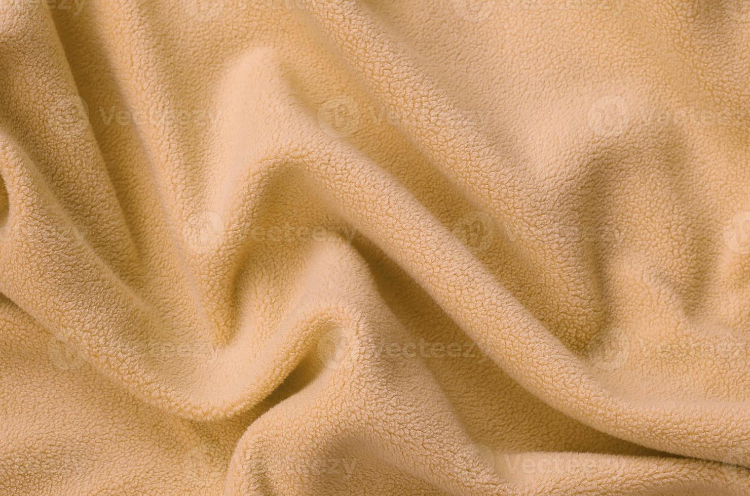The blanket of furry orange fleece fabric. A background of light orange soft plush fleece material with a lot of relief folds photo
