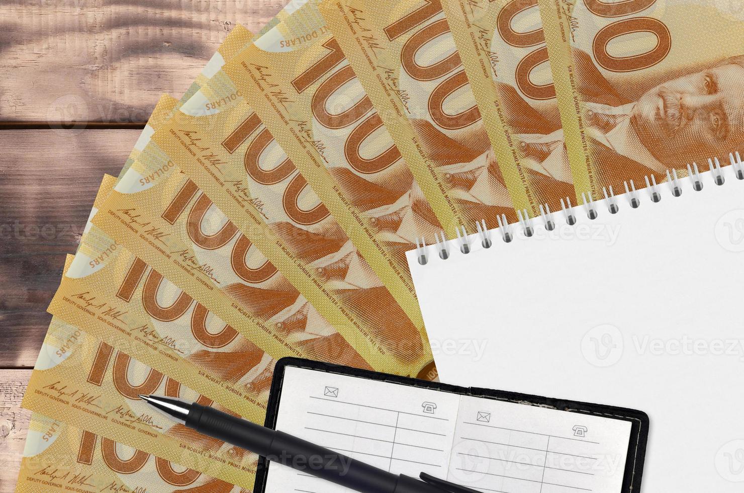 Ventilador de billetes de 100 dólares canadienses y bloc de notas con libreta de contactos y bolígrafo negro. concepto de planificación financiera y estrategia empresarial foto