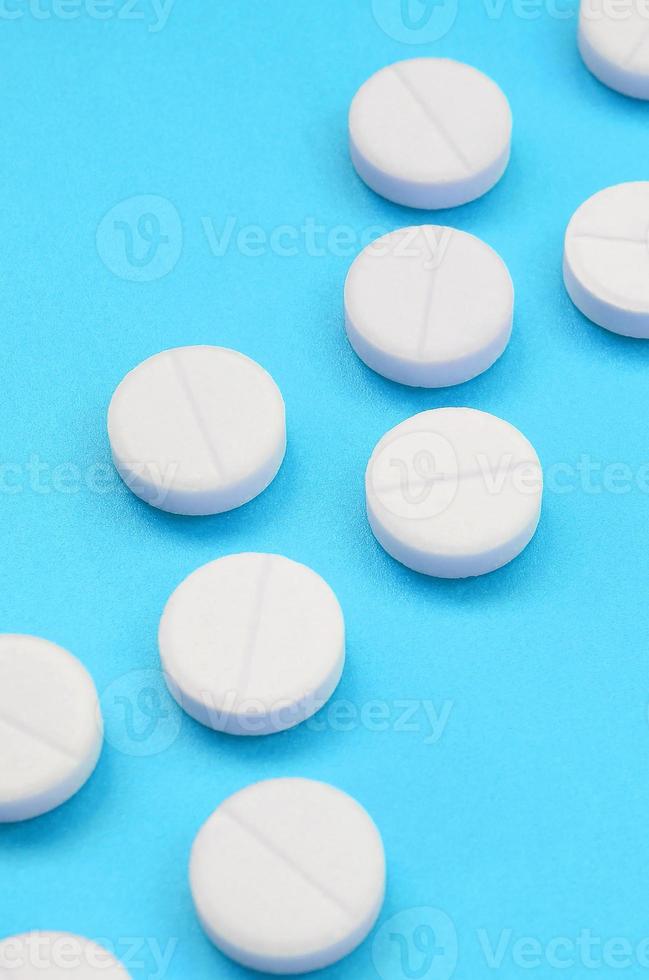 unas pocas tabletas blancas yacen sobre una superficie de fondo azul brillante. imagen de fondo sobre temas médicos y farmacéuticos foto