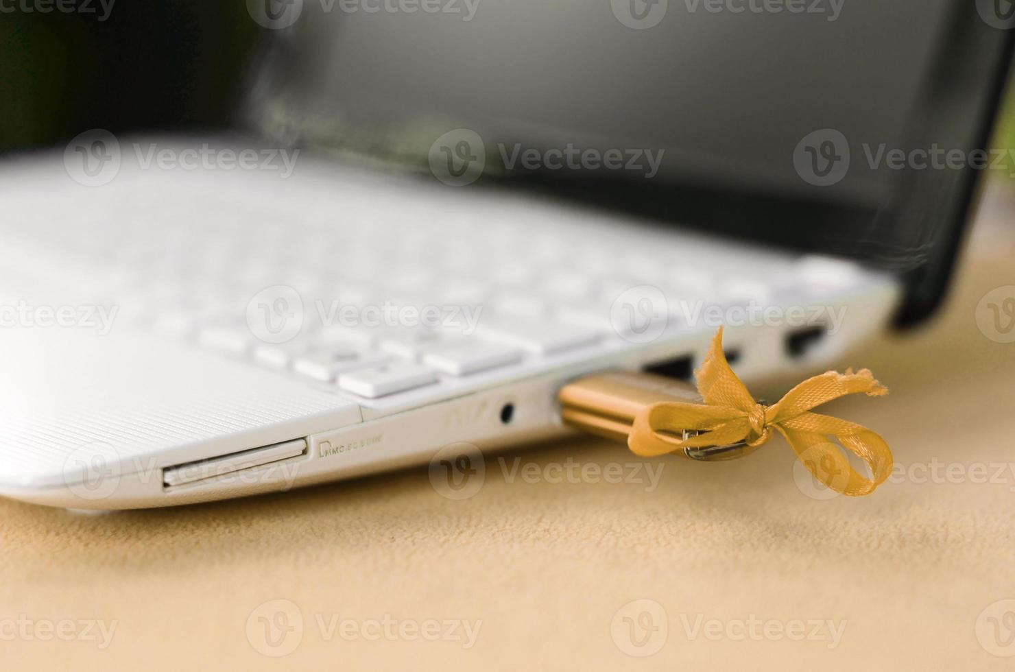 An orange USB flash drive with a bow is connected to a white laptop, which lies on a blanket of soft and fluffy light orange fleece fabric. Classic female design for a memory card photo