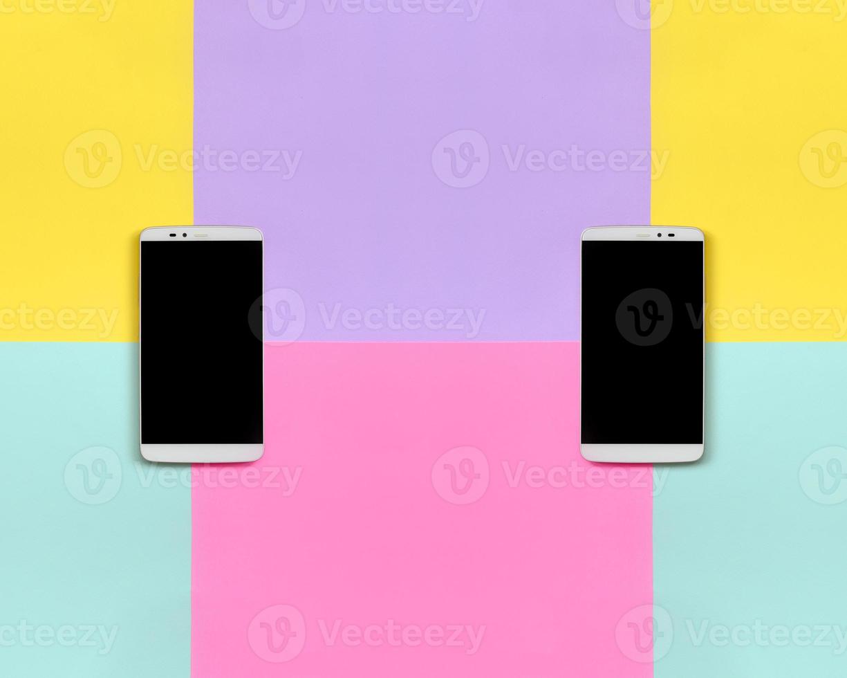 Two modern smartphones with black screens on texture background of fashion pastel blue, yellow, violet and pink colors paper in minimal concept photo