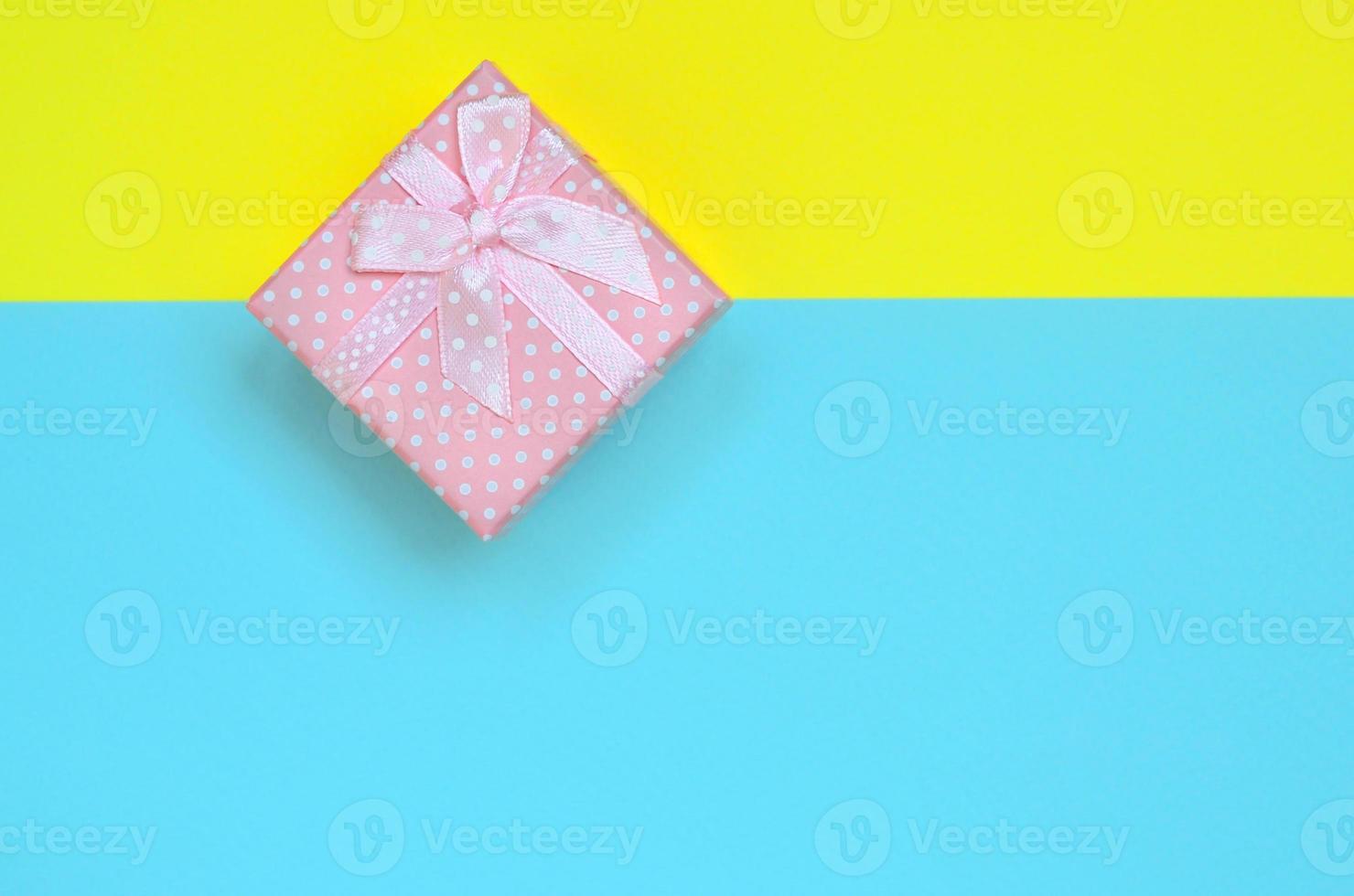 Small pink gift box lie on texture background of fashion pastel blue and yellow colors paper in minimal concept photo