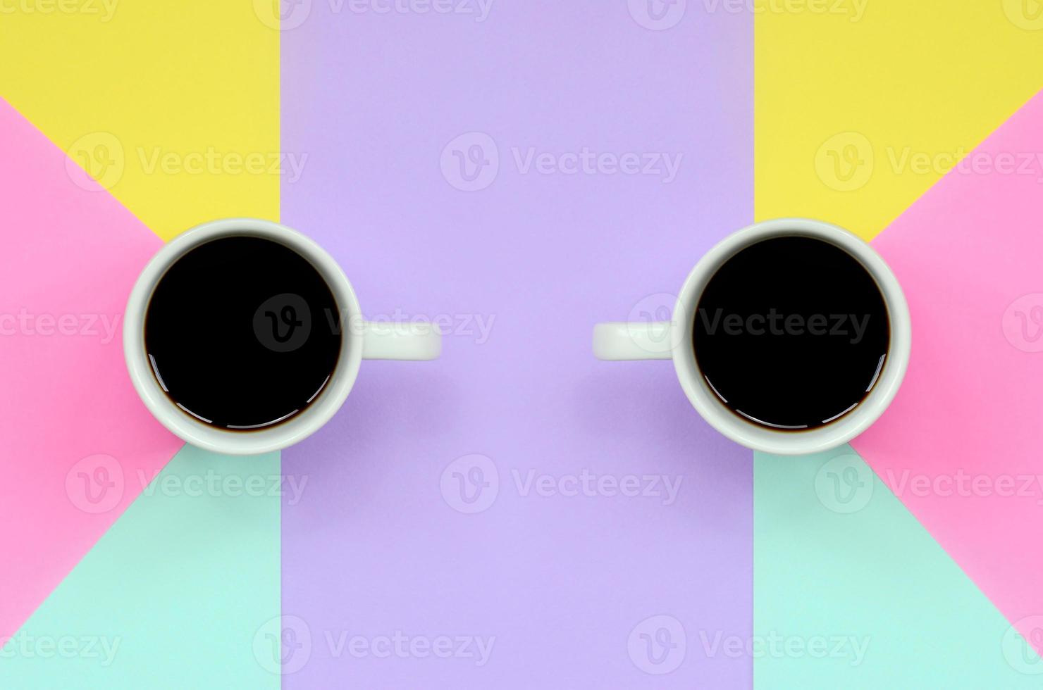 Two small white coffee cups on texture background of fashion pastel blue, yellow, violet and pink colors paper in minimal concept photo