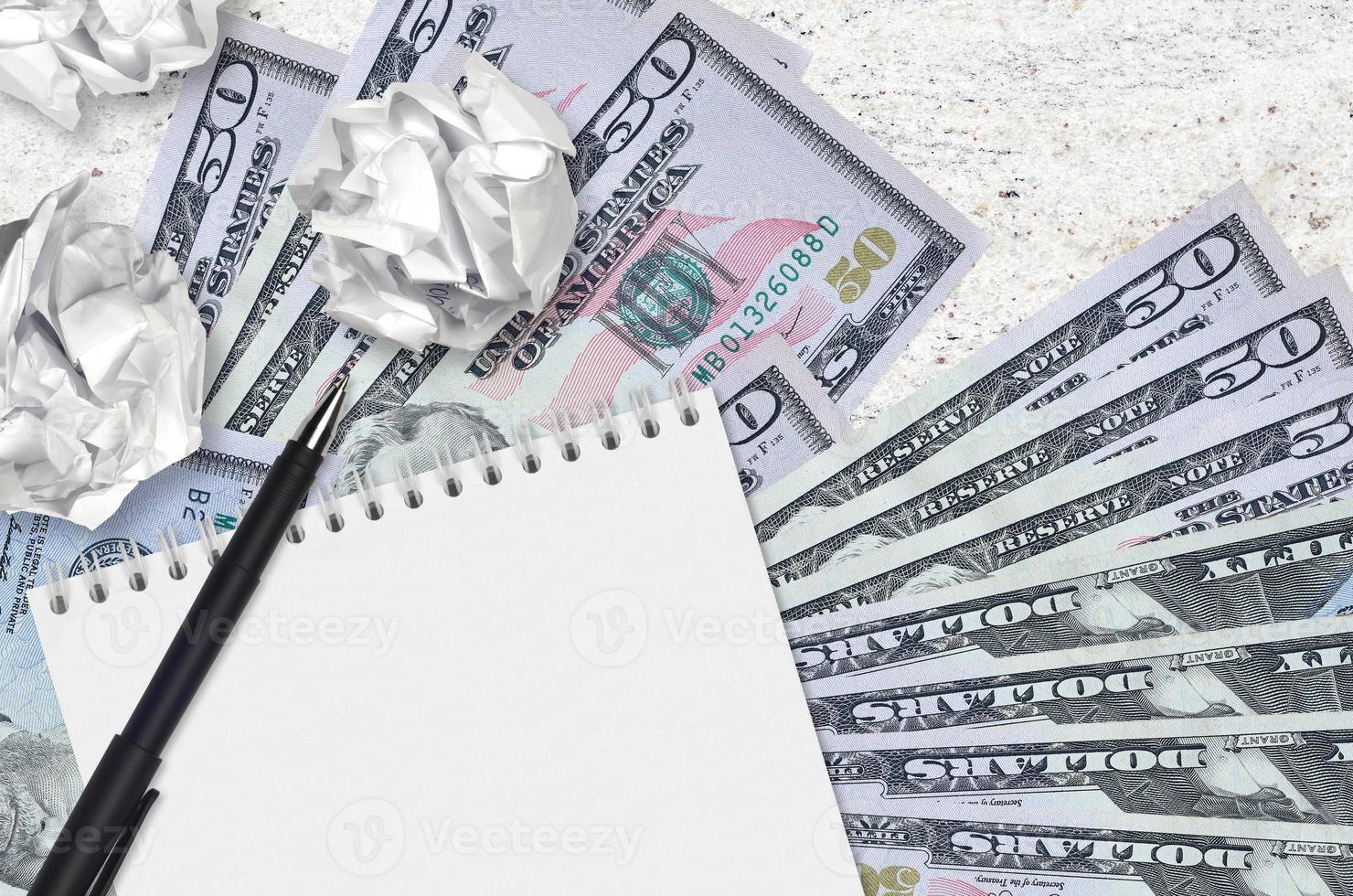 50 US dollars bills and balls of crumpled paper with blank notepad. Bad ideas or less of inspiration concept. Searching ideas for investment photo