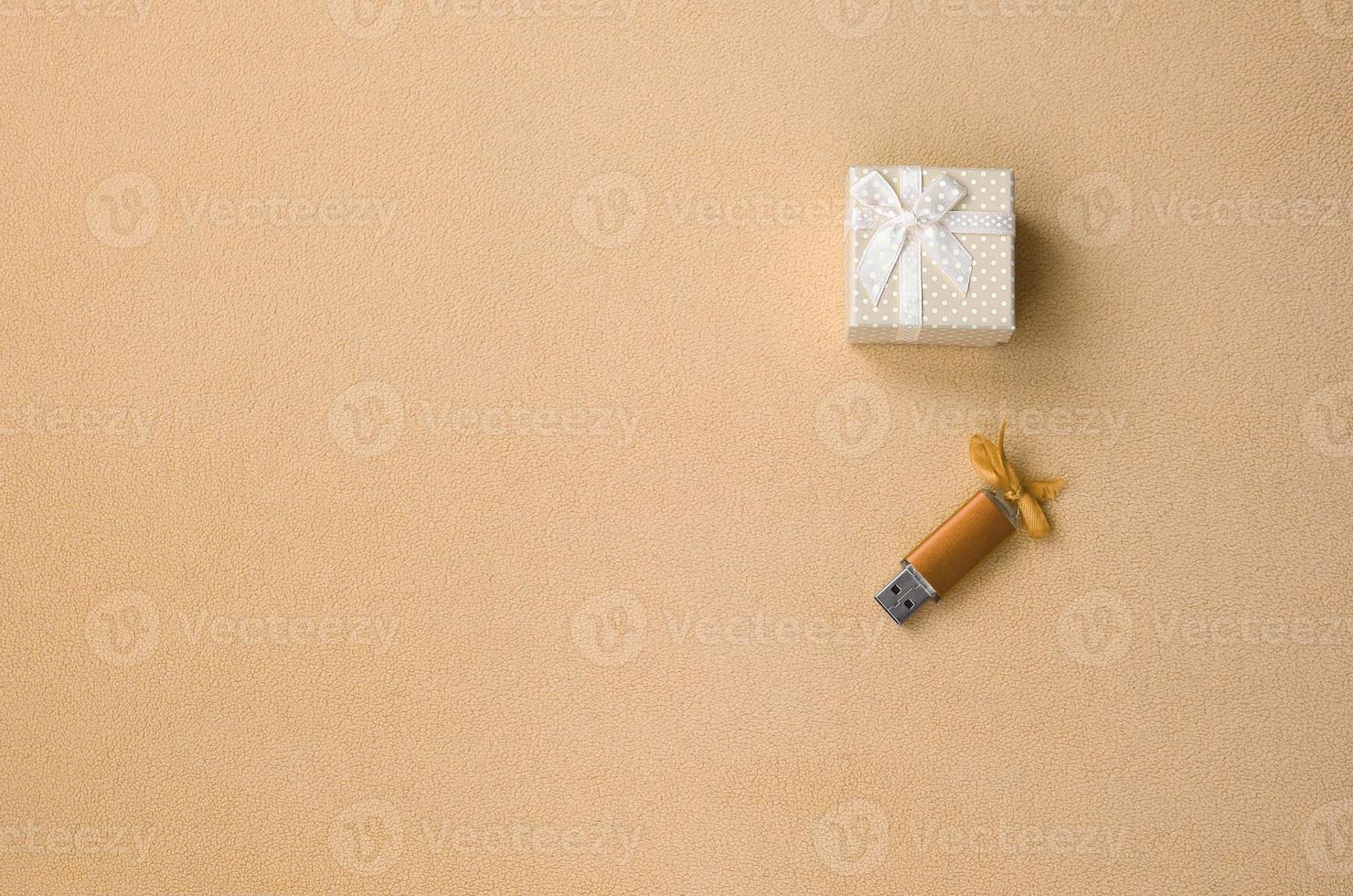 Orange usb memory card with a bow lies next to a small gift box in orange with a small bow on a blanket of soft and furry light fleece fabric. Classic fashion gift memory card design photo
