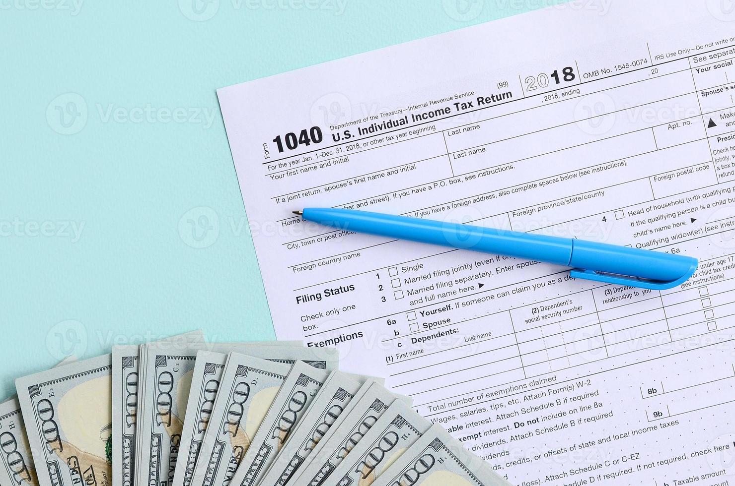 1040 tax form lies near hundred dollar bills and blue pen on a light blue background. US Individual income tax return photo