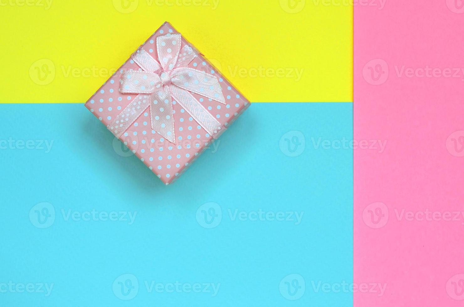 Small pink gift box lie on texture background of fashion pastel blue, yellow and pink colors paper in minimal concept photo