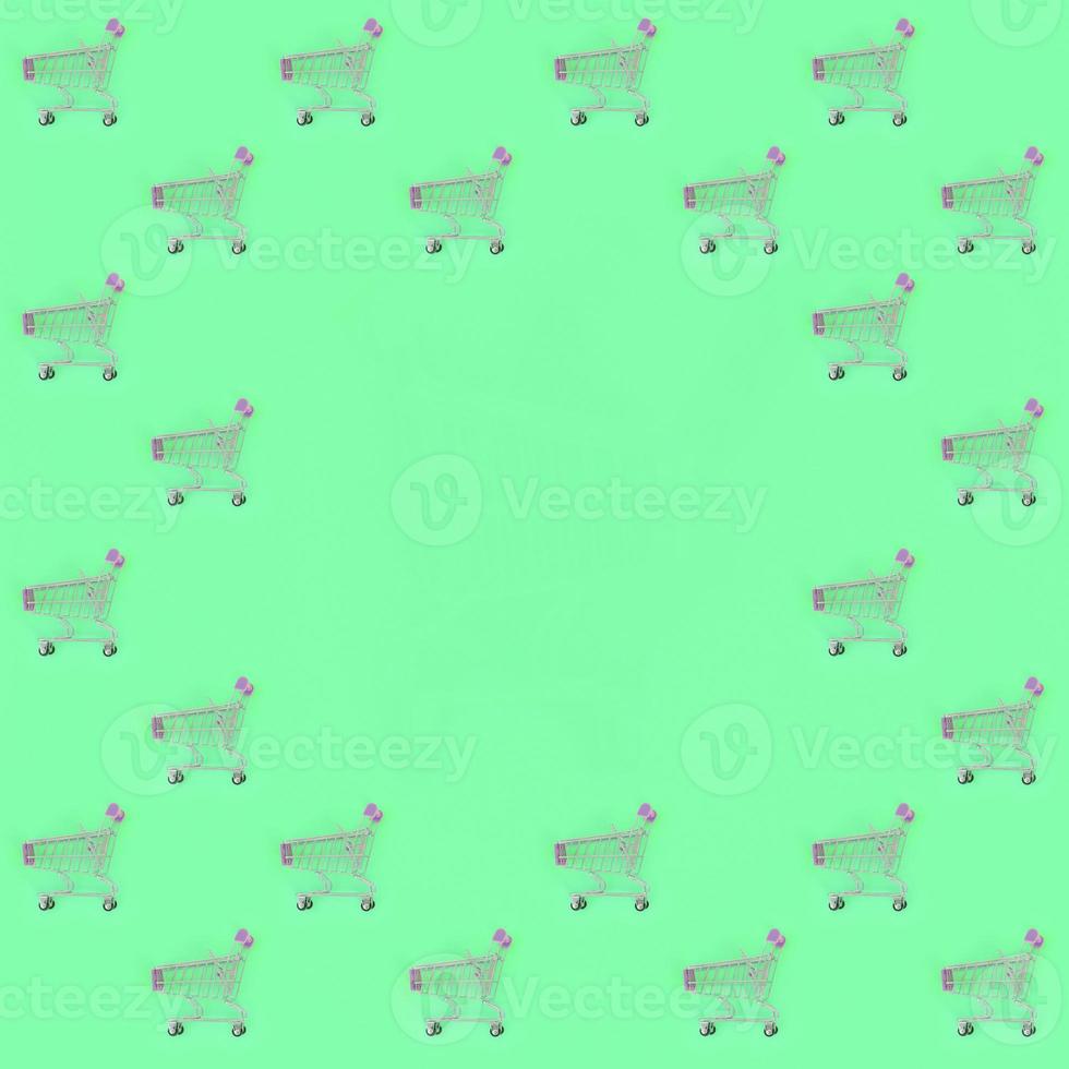 Shopping addiction, shopping lover or shopaholic concept. Many small empty shopping carts perform a pattern on a pastel colored paper background. Flat lay composition, top view photo