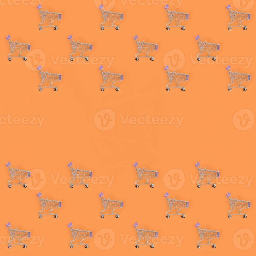 Shopping addiction, shopping lover or shopaholic concept. Many small empty shopping carts perform a pattern on a pastel colored paper background. Flat lay composition, top view photo