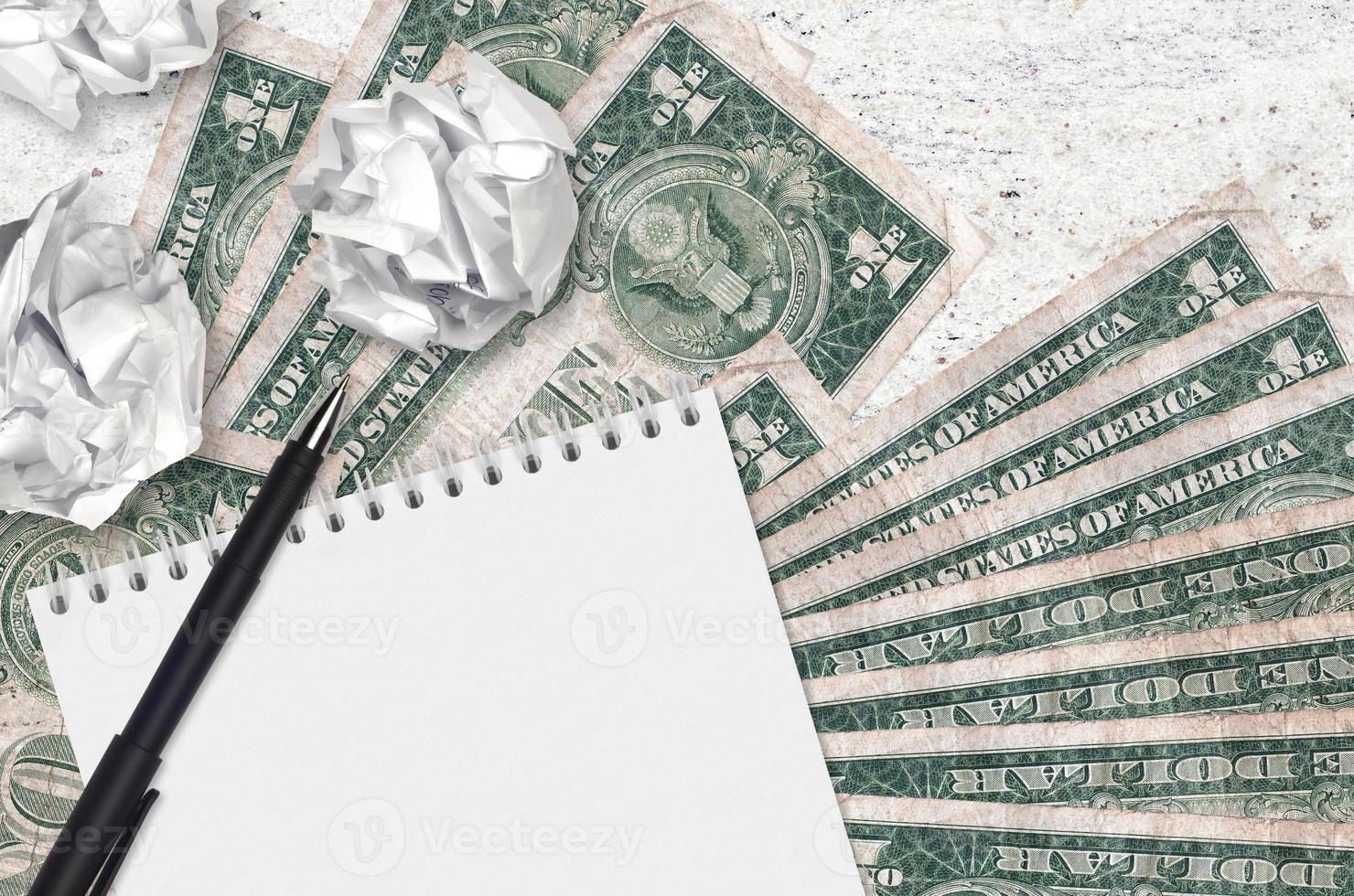 1 US dollar bills and balls of crumpled paper with blank notepad. Bad ideas or less of inspiration concept. Searching ideas for investment photo