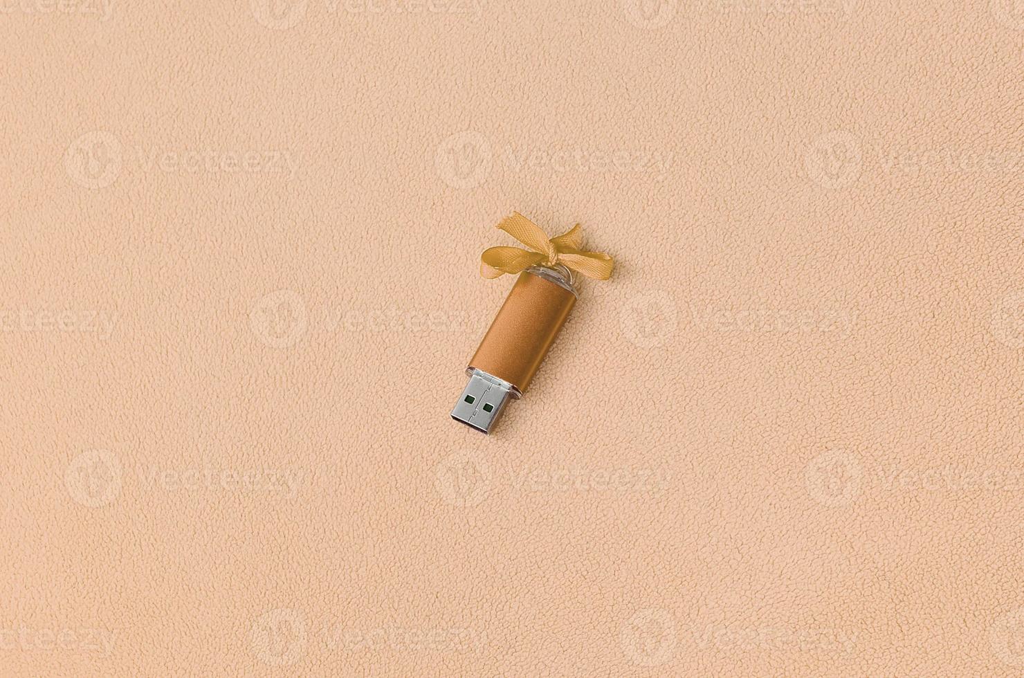 la tarjeta de memoria flash usb naranja con un lazo se encuentra sobre una manta de tela suave y peluda de color naranja claro. diseño de regalo femenino clásico para una tarjeta de memoria foto