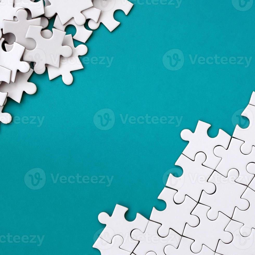 Fragment of a folded white jigsaw puzzle and a pile of uncombed puzzle elements against the background of a blue surface. Texture photo with space for text