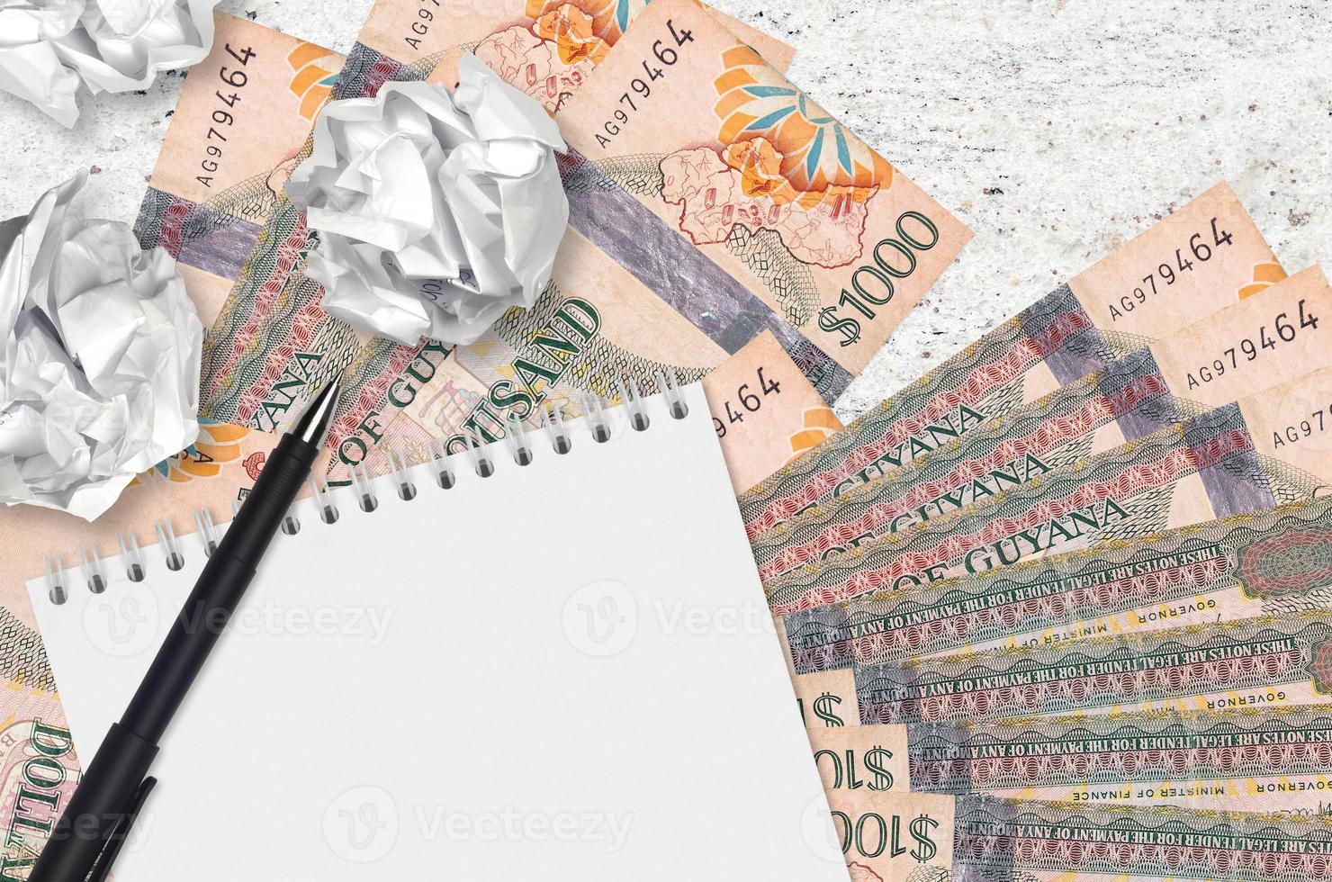 1000 Guyanese dollars bills and balls of crumpled paper with blank notepad. Bad ideas or less of inspiration concept. Searching ideas for investment photo