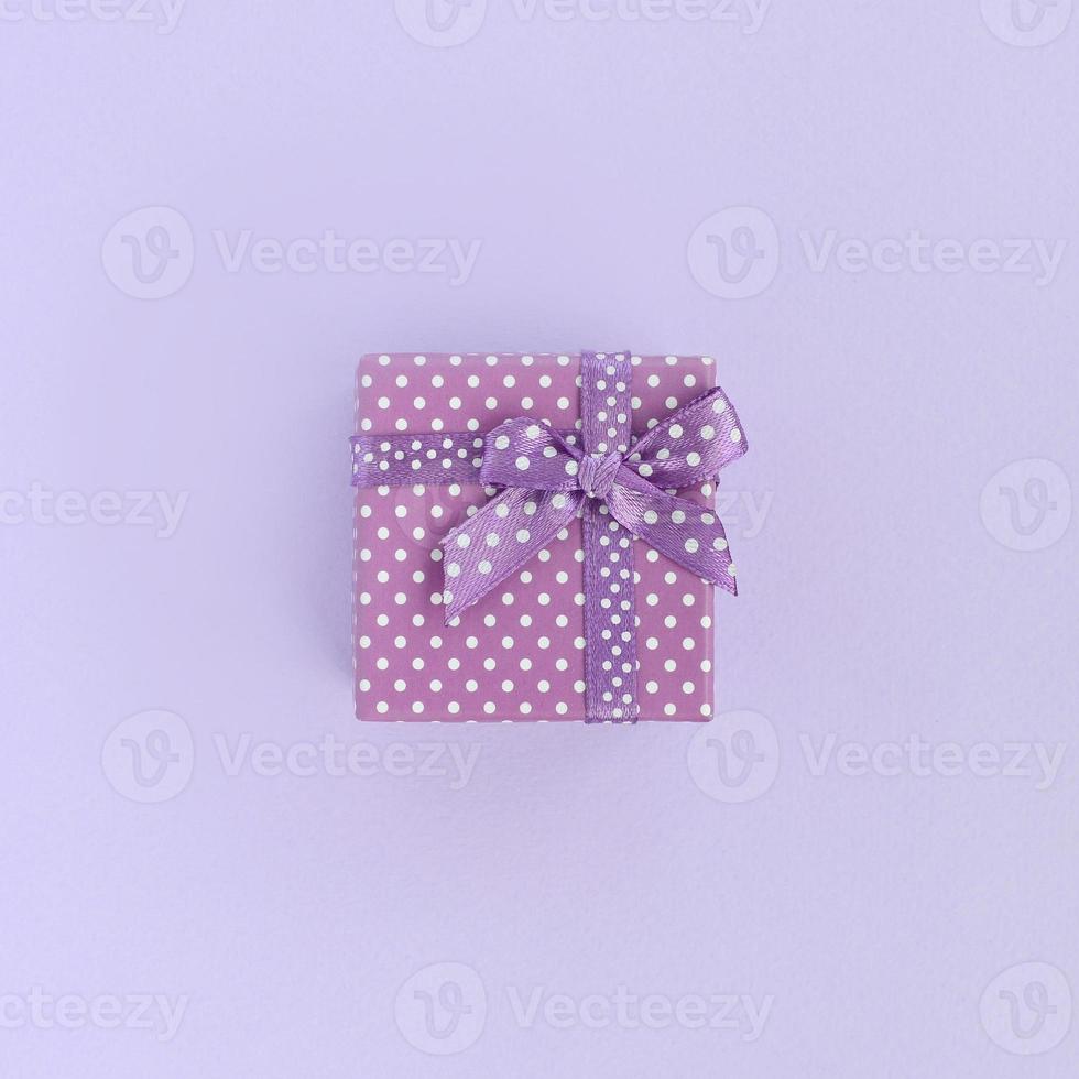 Small purple gift box with ribbon lies on a violet background. Minimalism flat lay top view photo