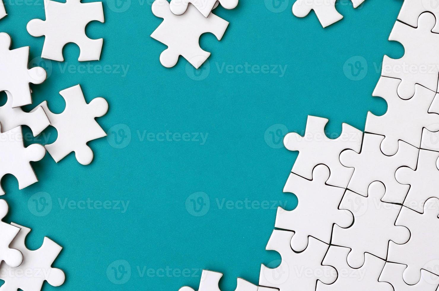 Fragment of a folded white jigsaw puzzle and a pile of uncombed puzzle elements against the background of a blue surface. Texture photo with space for text