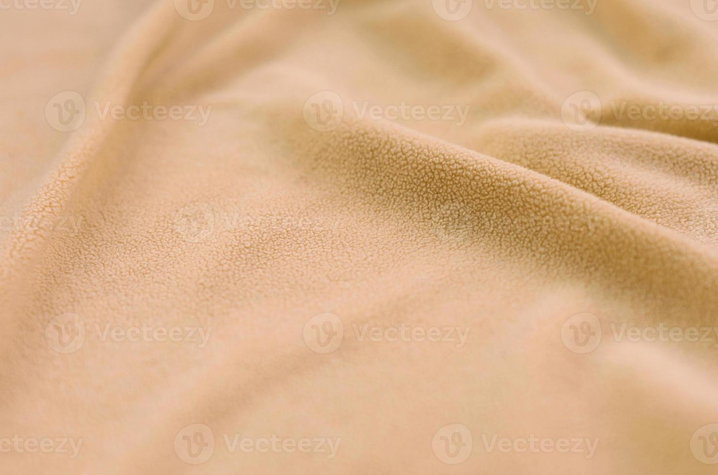 The blanket of furry orange fleece fabric. A background of light orange soft plush fleece material with a lot of relief folds photo
