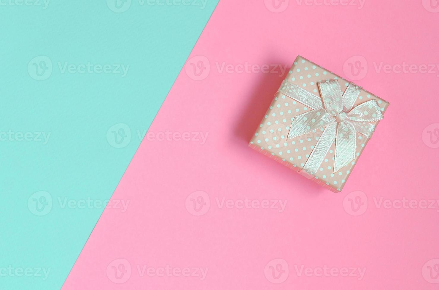 una pequeña caja de regalo rosa se encuentra en el fondo de textura de papel de colores azul pastel y rosa de moda en un concepto mínimo foto