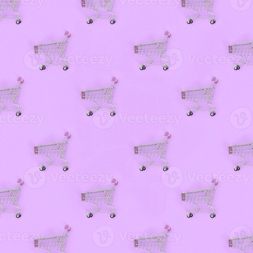 Shopping addiction, shopping lover or shopaholic concept. Many small empty shopping carts perform a pattern on a pastel colored paper background. Flat lay composition, top view photo