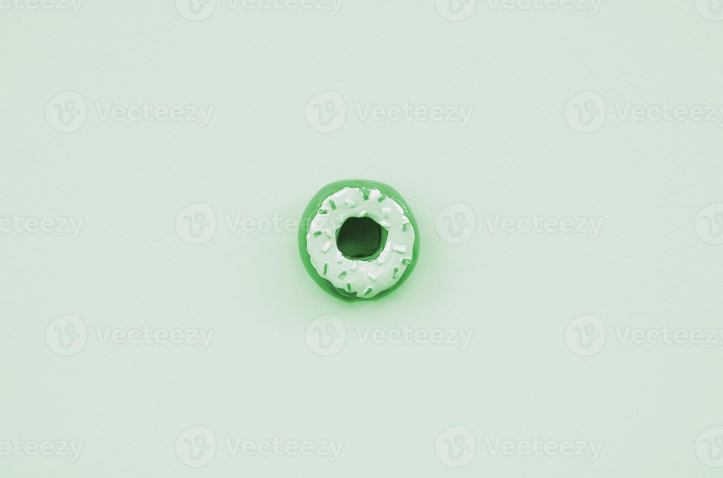 Single small plastic donut lies on a pastel colorful background. Flat lay minimal composition. Top view photo