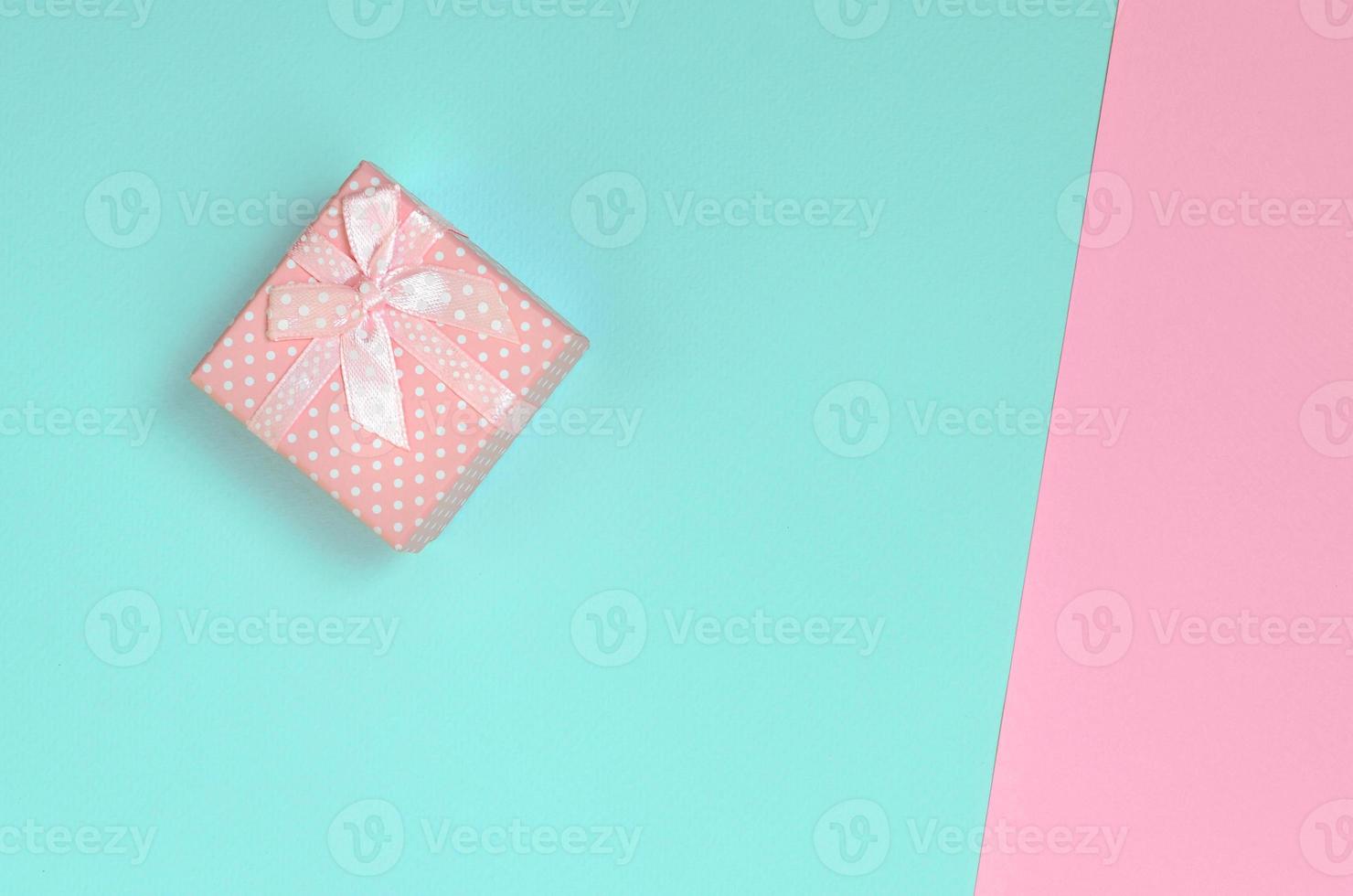 una pequeña caja de regalo rosa se encuentra en el fondo de textura de papel de colores azul pastel y rosa de moda en un concepto mínimo foto