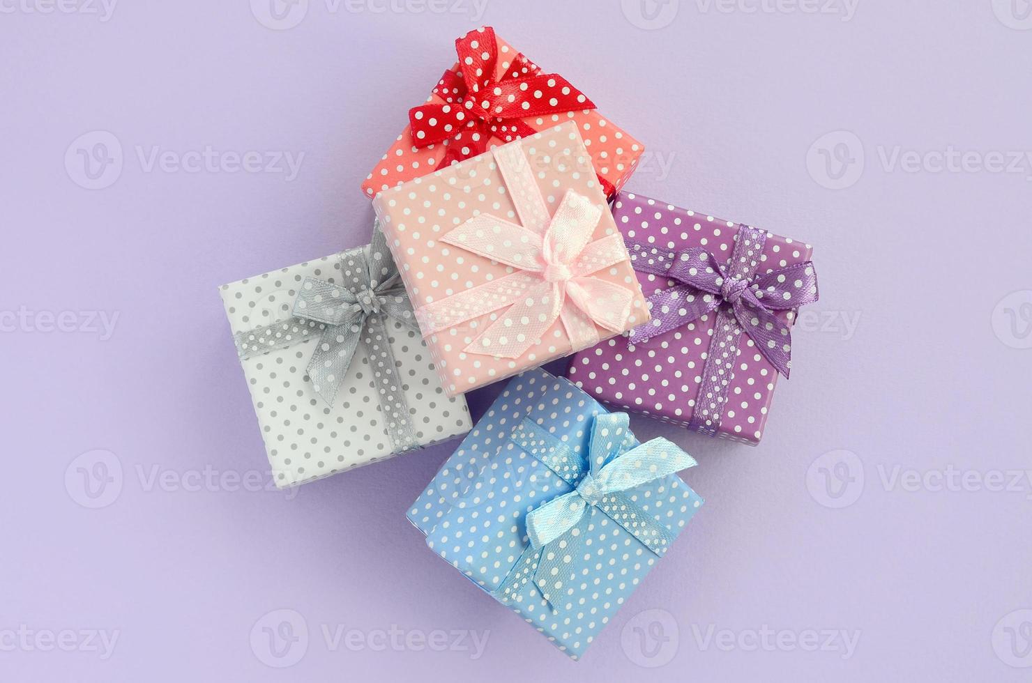 Pile of a small colored gift boxes with ribbons lies on a violet background. Minimalism flat lay top view photo