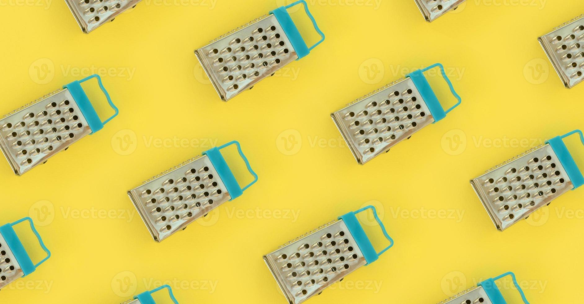 Small stainless steel graters lies on a pastel colored paper. Kitchen accessories. Tools for cooking. Flat lay top view photo
