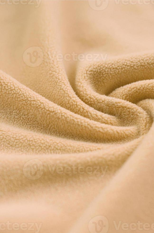 The blanket of furry orange fleece fabric. A background of light orange soft plush fleece material with a lot of relief folds photo