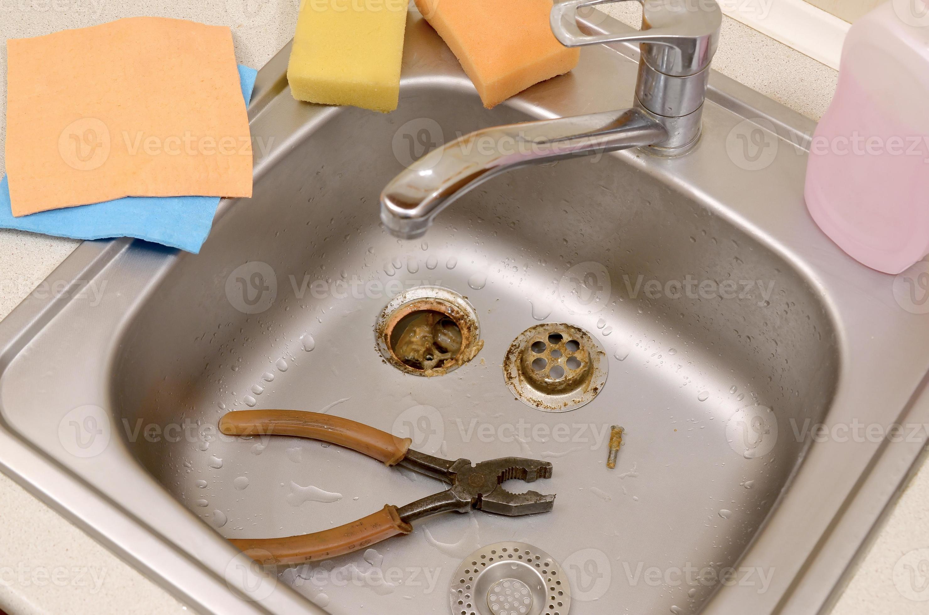 Pliers inside the silvery kitchen sink with a disassembled protective