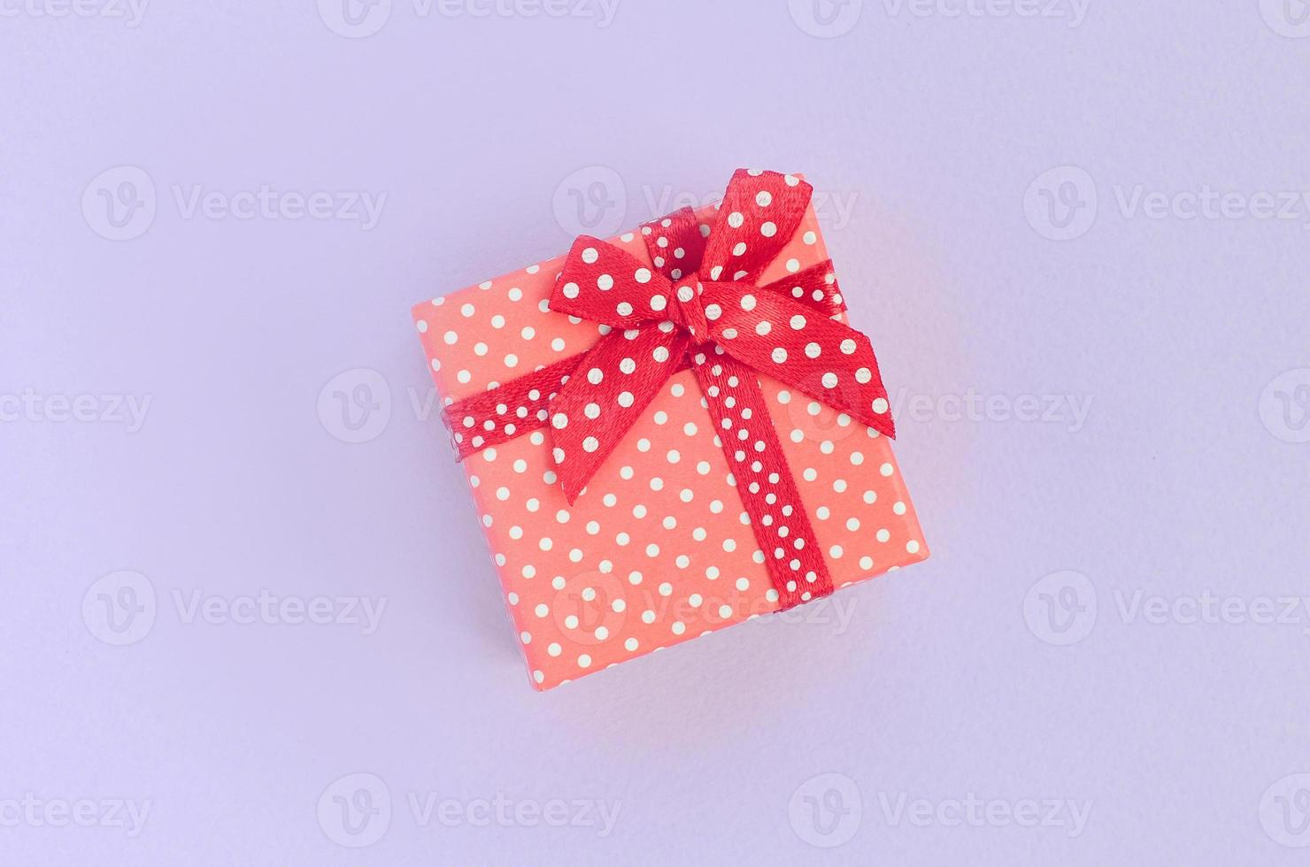 Small red gift box with ribbon lies on a violet background. Minimalism flat lay top view photo